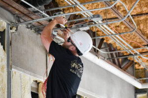 A man wearing a hard hat is installing materials on a ceiling, focused on his work in a construction environment.